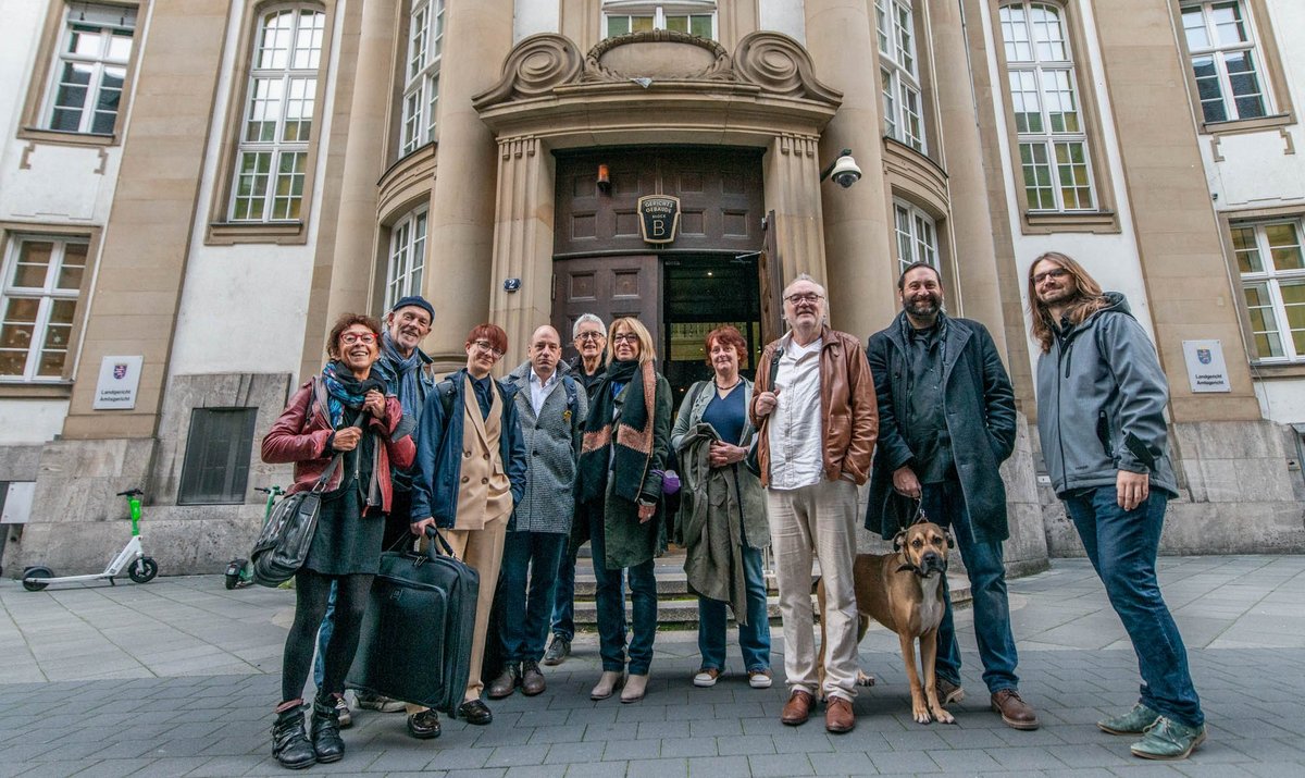 Vor dem Landgericht Frankfurt (von links): Kontext-Vorstand Anni Endress,  Unterstützer Klaus Schäffer, die Anwält:innen Anja Niederhofer und Markus Köhler, Kontext-Vorstand Jürgen Klose, aus der Kontext-Redaktion Susanne Stiefel, Anna Hunger und Josef-Otto Freudenreich, Unterstützer Steffen Braun mit Hund Clyde und Kontext-Redakteur Minh Schredle. Foto: Jens Volle