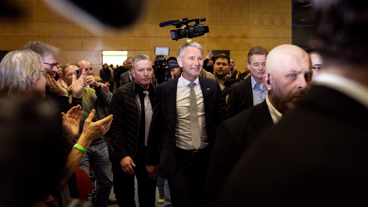 Höcke bei seinem Einlauf in die Halle, umrahmt von Sicherheitsleuten.mrahmt von Sicherheitsleuten.