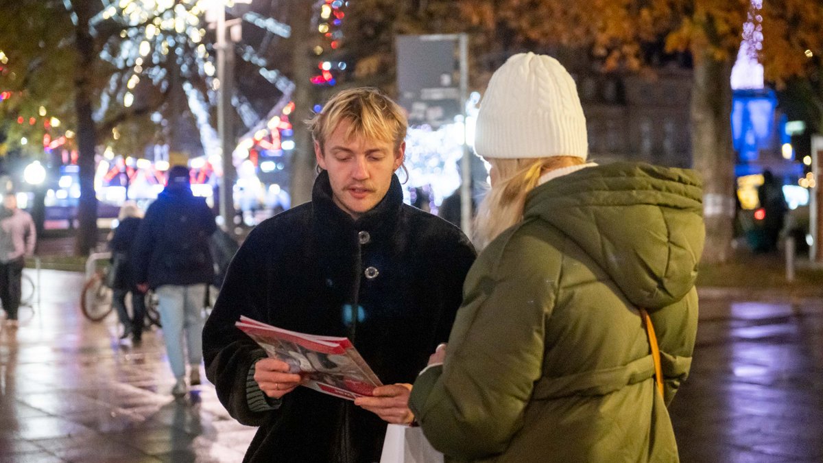 Er versucht die Straßenzeitung an Passant:innen zu verkaufen. 