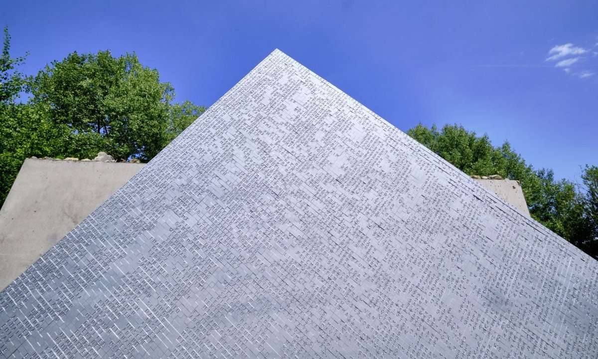 Der Ellwangener Künstler Rudolf Kurz goss alle Namen in zufälliger Reihenfolge in Aluminium, das Material des Flugzeugbaus. Dahinter steht eine kalte, schwere Betonwand. Von Hand mussten die Häftlinge im Winter 1944/45 Beton mischen und aufpassen, dass er nicht gefror.