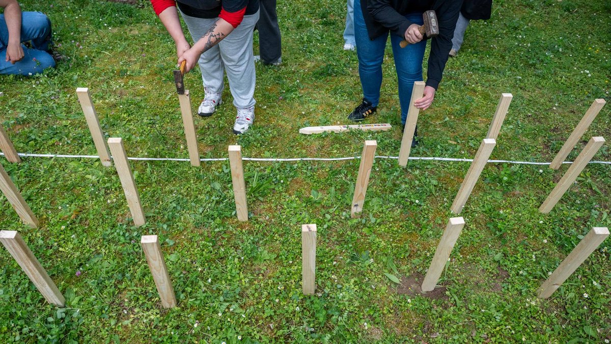 Gemeinsam klopfen sie die Hölzer in die Erde.