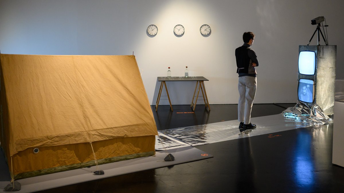 Eine Wasseruhr aus zwei Fernsehern, das obere Bild rinnt ins untere. Dort baut sich das Antlitz des Betrachters langsam auf.