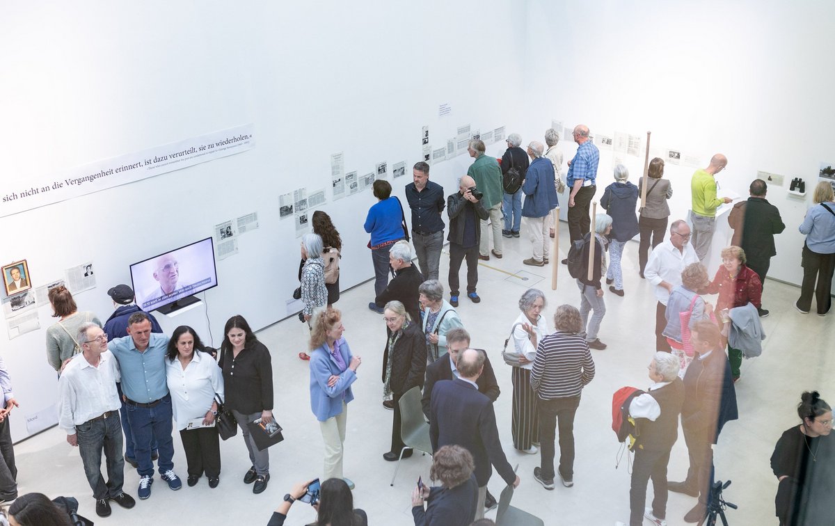 Rund 100 Besucher:innen sind zur Vernissage angereist. Vorne links, sich umarmend: Klaus Illi mit Sohn und Tochter Berishas und Übersetzerin.