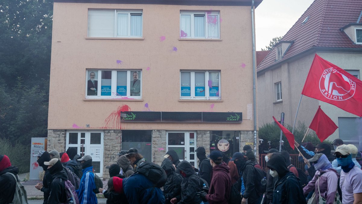 Das Büro wird mit Farbbeuteln beworfen, die Polizei zieht sich hinter das Tor zurück.