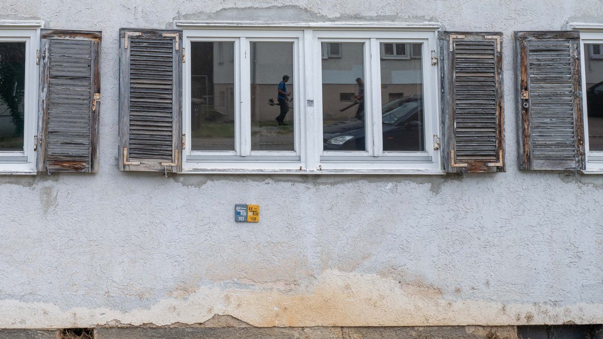 Das Renovieren hat sich die Eigentümerin gespart – immerhin ist der Rasen gemäht und das Laub weggeblasen, im Fenster spiegeln sich die Akteure.