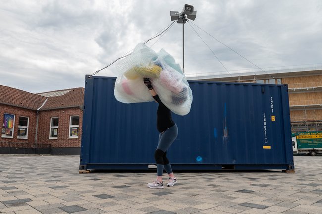 Kira Senkpiel schultert den Plastikmüll vor dem Container.  v