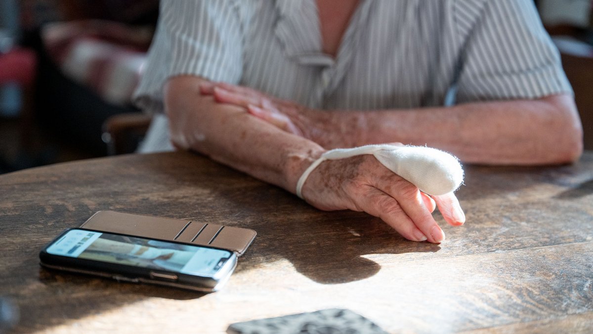 Edith S. erzählt, sie sitzt an einem Tisch in ihrem Wohnzimmer. Bilder auf ihrem Handy veranschaulichen ihre Geschichte. Foto: Jens Volle