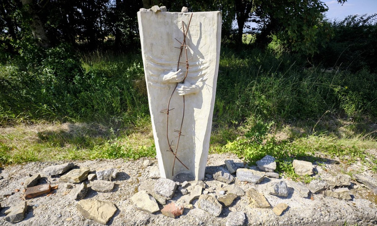 Skulptur "Mantel des Schweigens", umrahmt von Steinen mit den Namen von KZ-Insassen in griechischer Schrift.