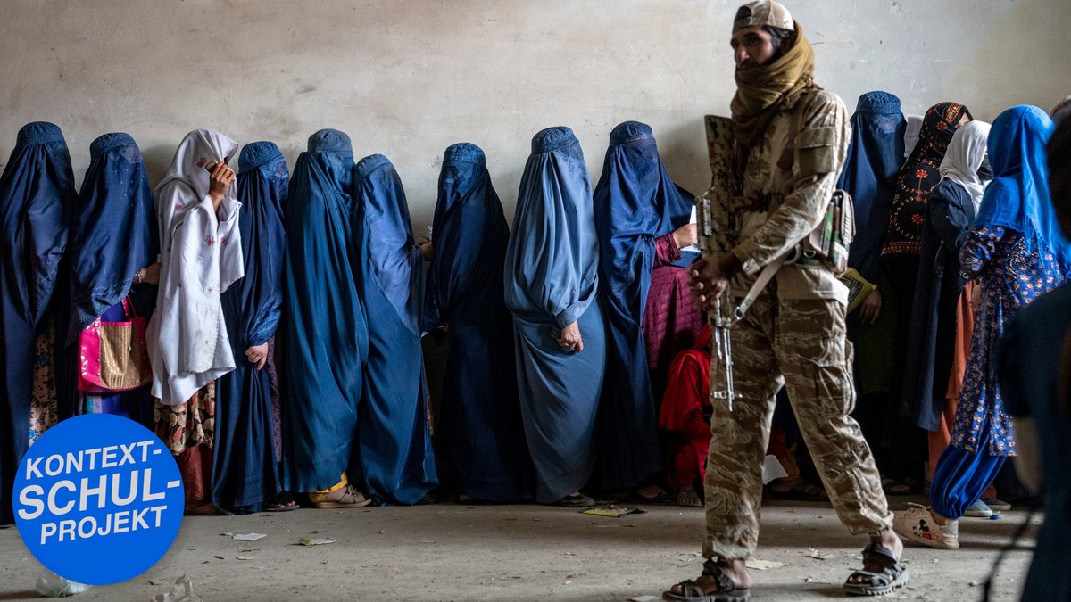 Frauen warten auf die Verteilung von Lebensmitteln durch eine Hilfsorganisation, bewacht von einem Talibankämpfer. Kabul, Mai 2023. Foto: Picture Alliance/AP, Ebrahim Noroozi