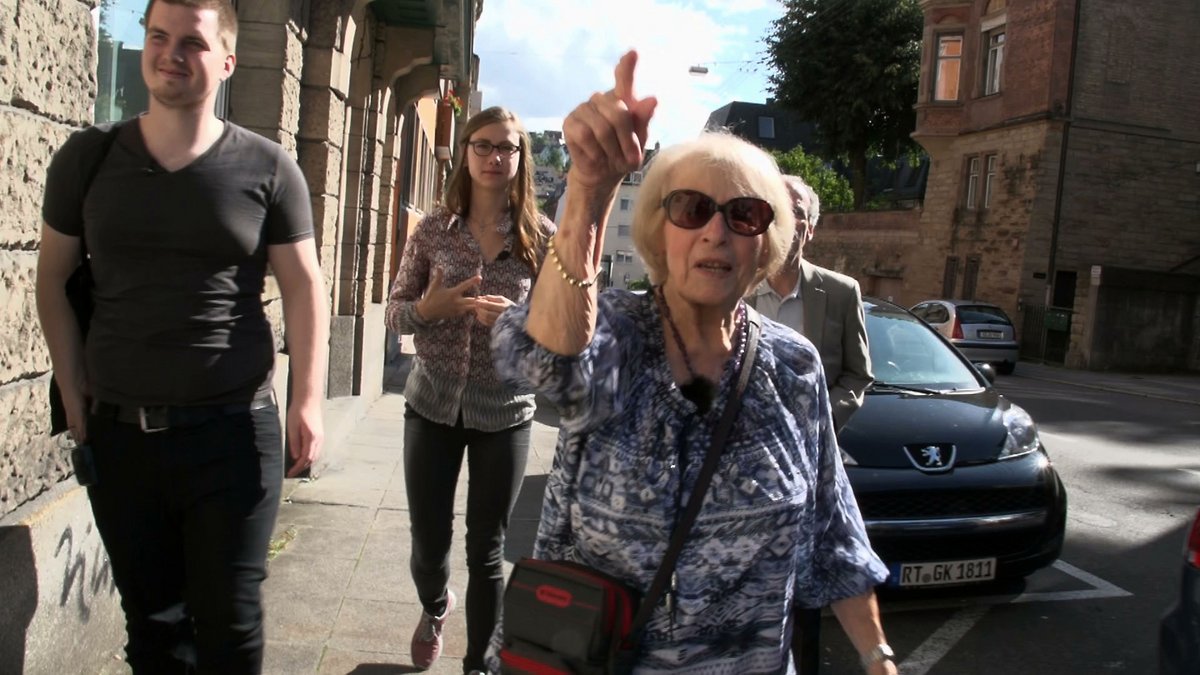 Charlotte Isler im Jahr 2014 vor dem früheren Wohnhaus ihrer Großmutter in der Stuttgarter Hohenstaufenstraße, zusammnen mit den Schüler:innen Fabian Brüssow und Sarah Haide. Filmstill: Steffen Kayser/Traube47