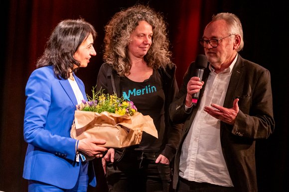 Blumentöpfchen aus Öko-Anbau für die Grüne, überreicht von Annette Loers, Merlin, und Josef-Otto Freudenreich, Kontext.