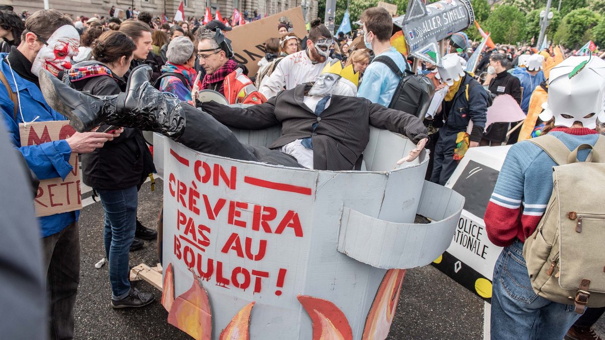 Mit papiernem Feuer unterm Kochtopf, auf dem steht: "Wir werden nicht auf Arbeit sterben", ...