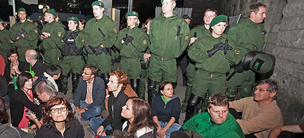 Illustre Blockadegruppe vor dem Nordflügel am 30. Juli 2010: ganz links vor der Polizeikette Brigitte Lösch, in der Mitte im blauen Sakko Werner Wölfle, rechts neben ihm Hannes Rockenbauch, im grünen Polohemd Jochen Stopper, neben ihm an der Mauer Bernd Riexinger, vorne links mit Brille Clarissa Seitz. Foto: Roland Hägele