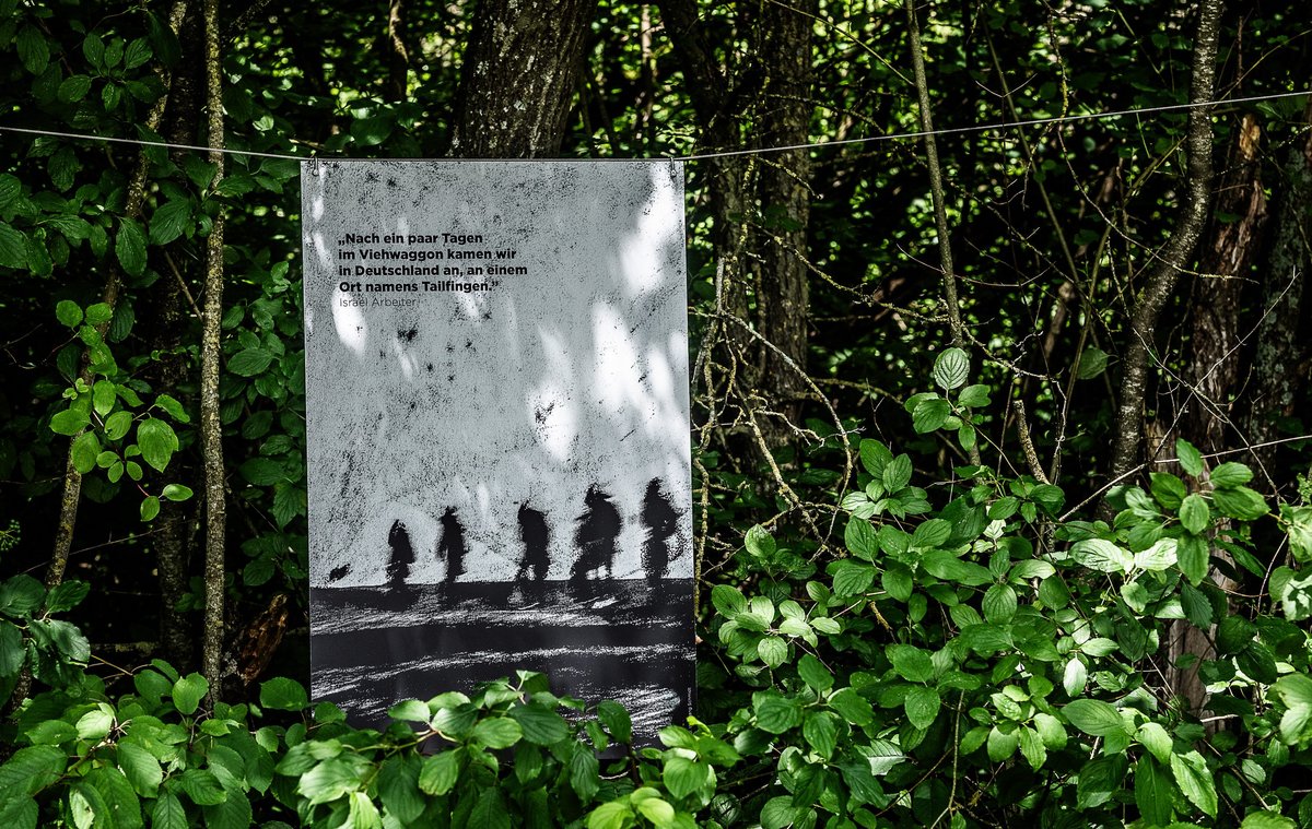 Ankunft im KZ-Außenlager: Ein Plakat irrlichtert aus dem Schatten der Bäume ins Heute herüber.